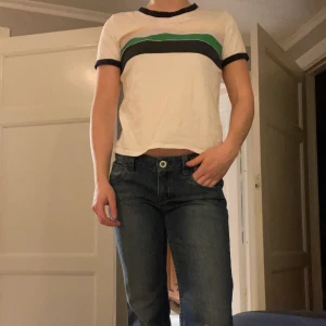 T-shirt med ränder  - Vit T-shirt med mörkblåa kanter och sträck med färgerna gul, lila, grön och marinblå. Från monki. Strl S