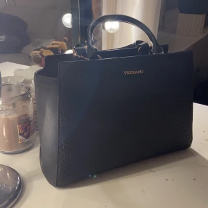 Vezzano väska helt ny!✨ - Superfin svart Vezzano väska inköpt på accent i Linköping för då ca 700kr . Väskan har inte använts alls då jag hade en annan. Ca 25cm hög och 30 cm bred, ganska rymlig och har fack inuti! Det långa bandet på väskan är avtagbart. 
