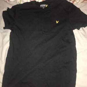 T-shirt är svart och det står med gult lyle scott märket