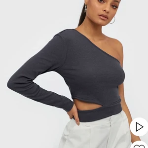 Nelly One Sleeve Cut Top - Jättefin mörkgrå one shoulder-topp med en cool detalj nertill!  Superbra till fest!! Använd ett fåtal gånger, är i nyskick. Helt slutsåld på hemsidan! Köptes förra året för ungefär 300 kr, säljer nu för 150 kr💓💓 Hör av dig vid minsta lilla fråga! 