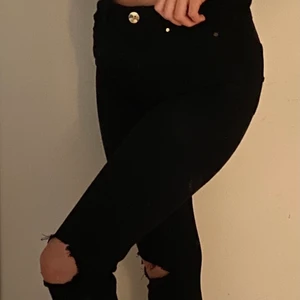 Svarta jeans med hål - Svarta jeans med hål i knäna. Köpta på H&M och är i stolek 34, men skulle säga att de passar S-M då de är väldigt stretchiga. Den har dragkedja och knapp i guldfärg i midjan samt fickor både fram och bak. Haft ett tag men de är ändå i bra skick. Säljer pga att de är lite för stora för mig. Kan mötas i Umeå eller skicka om köpare står för frakt. Spårbar: 66kr, icke-spårbar: 30kr