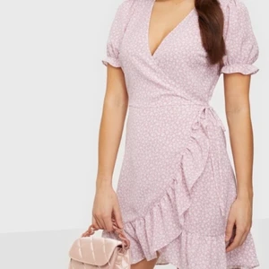 NLY Trend klänning i strl 40/42 - Omlottklänning från NLY Trend i färgen lila. Den har volangdetaljer, dold dragkedja samt knytband i sidan för att kunna justera passformen utifrån hur man vill ha den. Den är i nyskick och har används ett par få gånger. Nypris är 299kr, jag säljer för 50kr! Köparen står för frakt🤎