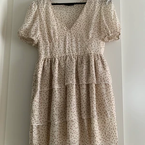 Klänning nyskick strl S - Prickig fin klänning i beiget. Volanger från midjan och ner samt formade kupor och puffärmar. Oanvänd!