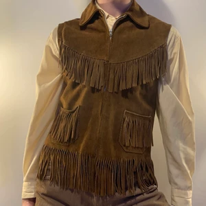 Vintage brun mocka cowboy väst fransar - Galen brun vintage mocka väst med fransarbåde på framsidan och baksidan och med fickor på framsidan 🐴 Denna västen sitter så bra och är så snygg nu til hösten med en stickad tröja under för en mer extra look! Släng på ett par bruna bootcut byxor eller bootcut jeans för den perfekta cowboy inspirerade outfiten! En så söt detalj är också den underbara tagen i nacken!