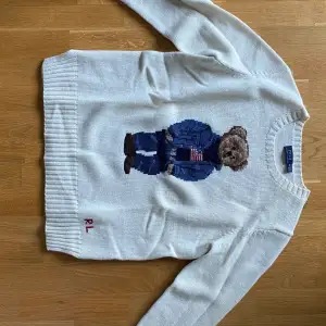 Vit stickad tröja från Ralph Lauren med nallebjörn på framsidan. Använd endast en gång så i mycket fint skick. Nypris 3600 kr. Säljes för 1400 kr exklusive frakt. 