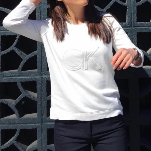 Vit tröja, Calvin Klein - Vit tröja från CK. Armlängd: går över armbågarna. I fint skick. 58% bomull, 42% polyester. Går finfint att stryka (ostruken på bild 2 och 3). Dåligt ljus på bild 2 och 3 också, men den är vit och inte beige/gulvit.