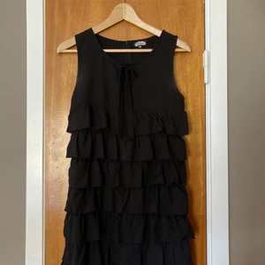 Snygg svart klänning med volanger XS - Svart klänning med snygga volanger och dragkedja 🖤 Knappt använd, men kan ana lite vitt i armhålan vilket ej syns på. Skriv om du undrar något ✨