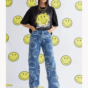 NYA Jeans Smiley® x H&M SLUTSÅLD stl.38  - Smiley® x H&M. Ett par 5-ficksjeans i tvättad bomullsdenim med tryckt mönster. Jeansen har hög midja och låg gren samt raka, vida ben. Gylf med dragkedja. De är för närvarande slutsålda överallt. Aldrig använts. Perfekt skick. Jag skulle säga att de är lite större i storleken som 38. Midjan är 70 cm. Inre längd är 78cm.