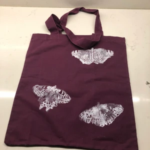 Tygkasse med fjärilstryck - Mörklila tygkasse i återvunnen bomull. Tryck med miljövänlig vit tryckfärg. Fjärilarna föreställer Aspfjäril, Sorgmantel och Makaonfjäril. Samfrakt möjligt.