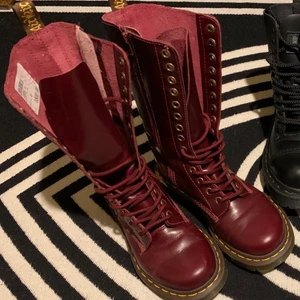 Dr Martens 14-håls vinröda - VINRÖDA 14-HÅLS UTAN STÅLHÄTTA SKICK: Helt nya, oanvända med prislapp kvar. Impulsköpta för över 10 år sedan och har inte blivit använda.  De har blivit lite knögliga efter att ha legat i en kartong i förrådet, lite användning och infettning lär göra susen! Ca 28cm höga, snörning samt dragkedja på sidan. Fler bilder finns.  (Nypris 1800kr) MATERIAL: Blank läder. OBS: katt finns i hemmet. 
