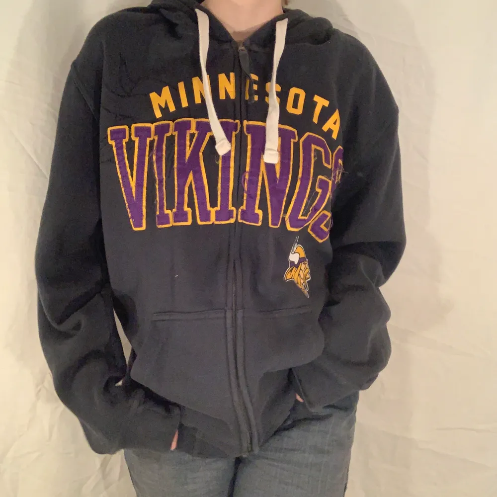 Mörkgrå hoodie med lila och gult tryck som läser Minnesota Vikings från NFL. Fint skick. . Hoodies.