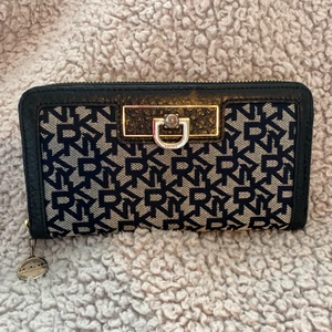 DKNY Plånbok  - Rymlig och lyxig plånbok från DKNY. I mycket fint skick bortsett från avskavd yta på metalldetalj och kedja, se bild 2 och 3. 