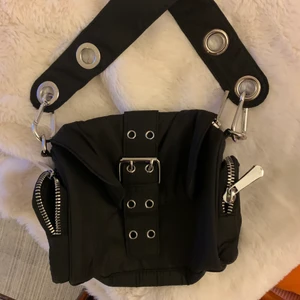 Svart Axelväska  - Svart axelväska med silverdetaljer, två fickor på sidorna med dragskedja och ett stort fack i mitten. 