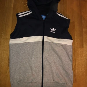Adidas väst - Adidas väst i kofta material med luva. Säljs pga att den är för liten för mig. Inga fel på den, andvänd endast 1 gång. Den är så gott som ny. Färgen: mörkblå,grå,vit. 