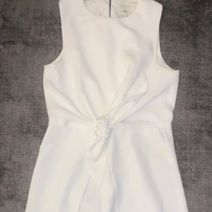 Vit byxdress med knut framtill - Vit byxdress med knut framtill, dragkedja och knapp där bak. Strl 12 år. Använd några gånger men bra kvalitet. Så fin och skön till sommaren. 
