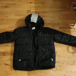 Härlig svart vinterjacka med reflexband - Härlig o varm jacka. Fint skick..dock lite trasig vid vänster ficka. Reflex över armar och luva