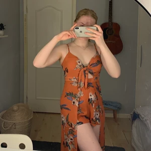 Jumpsuit med blommönster  - Kopparfärgad jumpsuit med blommönster från pull & bear. Plagget är i bra skick ändats används ett fåtal gånger. Jumpsuit framifrån och långklänning bakifrån. Köpare står för frakt.