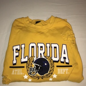 Långärmad tröja med ett Florida märke på. Använd ytterst lite. - En gul långärmad tröja med trycket ”Florida” tvärs över bröstet. Det är ”slitningar” över hela tröjan samt två vita sträck på båda ärmarna. Storleken är 36/S. 
