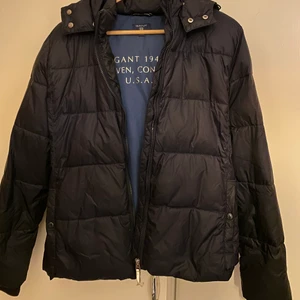 Dun jacka - Säljer denna superfina tunna dun jackan från Gant, köptes på Kidsbrandstore för ca 3 år sedan men har inte används mycket alla och är i väldigt bra skick!❤️‍🔥 Avtagbar luva. Den är mörkblå! Perfekt till våren! Den är i storlek 170/15 år och skulle säga att den passar S💘