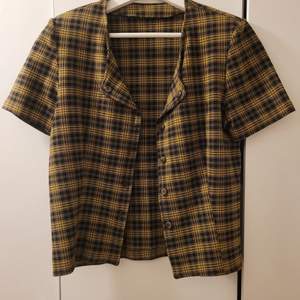 En gul brun rutig kortärmad tröja/kavaj med axelvaddar. Den är köpt secondhand men ser ny ut