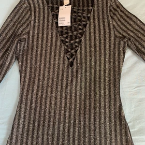 Tröja med snörning  - En helt oanvänd svart/grå glittrig tröja med snörning. storlek S men passar M också, taggen sitter kvar. 100kr om vi möts i Kalmar, annars 120kr.