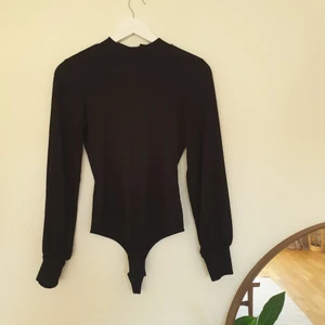 Svart långärmad body, stl M - Svart, lätt ribbad, stringbody från Y.A.S, stl M. Söt knappdetalj i nacken och lite puffiga ärmar. Frakt tillkommer. 