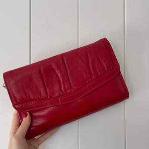 Röd handväska i fake läder. Jättegullig! Den har band med som man kan ta bort men också ha den som en axelremsväska. Har använt den ganska mycket men ser fortfarande väldigt bra ut! 