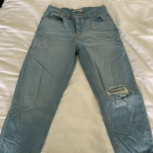 Levis mom jeans - Ett par Levis mom jeans i ljusblå jeansfärg med hål på ena knät som enligt mig sitter precis där man vill ha det. Går att både vika upp och rulla ner hela vägen. Storlek 29, passar mig som brukar vara storlek 40 i byxor. 