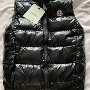 Moncler väst - Säljer en fin oanvänd moncler väst. (Se prislapp) Västen är identisk till den äkta. Finns en kod med som man kan scanna västen. Västen är i storlek M men är väldigt liten i storleken så den passar en storlek S eller Xs mer. 