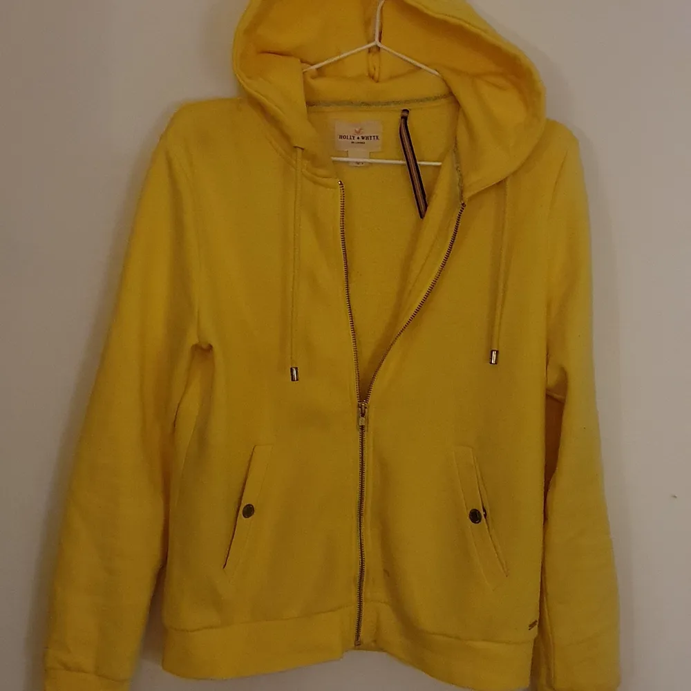 En zipup-hoodie från Holly & Whyte i en glad gul färg med guldfärgade detaljer. Sparsamt använd, inga fläckar eller liknande. Pris kan diskuteras vid snabb affär. Hoodies.