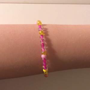 Ett armband i färgerna rosa lila och gul. Armbandet har bindes ringar och karbinhakar. Det är ett hemma gjort armband som jag tycker är super snyggt och fint. 🌸✨