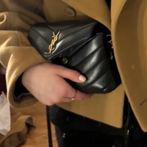 Yves saint Laurent loulou väska - Ysl väska i modellen loulou toy bag. Jätte fin och bra skick, lite repig på märket men inget man knappt lägger märke till. Har kvitto, dustbag och tag. Svart med guld detaljer