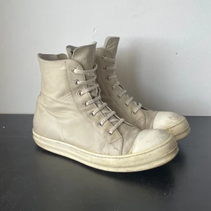fw16 mainline ramones - 100% äkta rick owens mainline höga ramones i deer skin. cream/milk färg. fw16 tyvärr ingen box. size 44. kom dm för fler bilder😵‍💫heeldrag, annars inga flaws 
