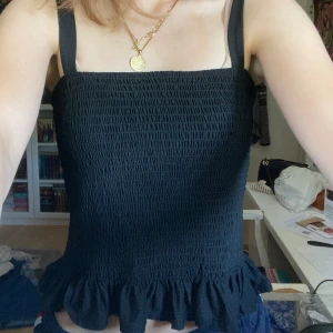 Svart stretchig topp med volang - Fin svart sommartopp med volang nertill. Nästintill nyskick! Har bara använt den ett fåtal gånger. Kan passa både XS och S.