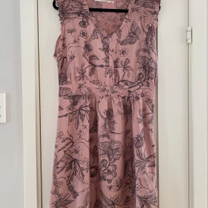 Rosa klänning med blommönster från Part two i strl 38. Modell Oleiz - Rosa klänning med blommönster från Part two i strl 38. Modell Oleize  Sparsamt använd och i fint begagnat skick.  Mått Över bröstet: ca 52 cm Längd från axeln och ner: ca 98 cm  61% viskos och 39% bomull 