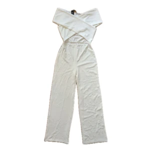 Byxdress / Jumpsuit Nelly  - Vit byxdress / jumpsuit från Nelly i storlek M. Oanvänd, prislapp kvar. Byxdressen är högmidjan och exponerar lite mage, följt av överdelen som korsas över bröstet. Kan mötas upp i Stockholm 