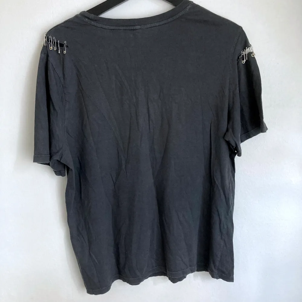 AC/DC t-shirt med säkerhetsnålar i följsamt material. Mått i cm: bröstvidd 50; axelbredd 41; längd fram från axeln 61; ärmlängd 22.. Skjortor.