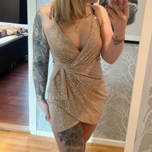 Guldig paljettklänning - Aldrig använd då jag köpte två och valde den andra sen blev de aldrig att jag skicka tillbaka den!  Man kan även sätta dit en säkerhetsnål för att förändra v-ringningen Dragkedja i ryggen, mindre slits framtill
