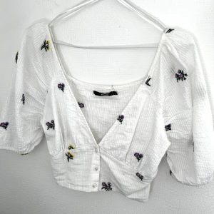 Sommarblus BikBok - En jättegullig vit sommarblus med blommor på ifrån Bikbok. Den har en V-ringning samt puffärmar💕 Har bara använt den 2 gånger💕