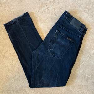 Nudie Jeans i modellen Sleepy Sixten och färgen ”Dry Black Selvage”, använda till en snygg wear och i gott skick. Storlek: 32 W, 32 L , Midja: 41.5 cm Ytterben: 103.5 cm Benöppning: 19 cm