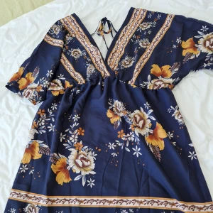 Söt blommig klänning, djup urringning bak. - Storlek small, oanvänd. Knytband i ryggen. Längd ovanför knä.