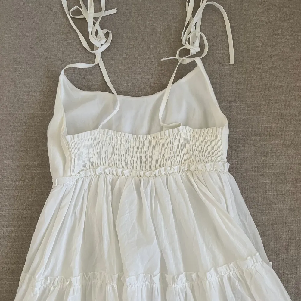 En fin vit klänning som knappt kommit till användning. Bra skick. Tunna släta band med möjlighet att knyta ut efter storlek. Ribbad där bak som gör att den sitter skönt i ryggen.. Klänningar.