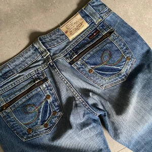 Superlågmidjade vintage y2k straightleg jeans med detaljer och stenar - Midja: 39 cm. Innerben: 80cm. Säljer dessa super snygga jeans med detaljer på fickorna med stenar och dragkedjor. Dom är tyvär för små på mig så har inga bilder på men måtten står. Fint skick och DRÖM vintage BRALLAN💋 tryck gärna på köp nu