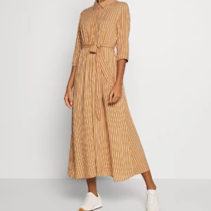 Brun klänning  - Andvänd men i bra skick. En brun klänning med vita ränder.