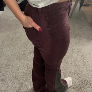 Leopardmönstrade jeans - Leopardmönstrade bootcuy jeans men låg midja, vinröd och gråa vid sidorna. Skulle säga att de är i storlek 34-36. Midjemått : 36cm rakt över. Innerbenet längd: 78cm. 