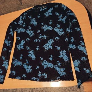 Tröja - Svart tröja med blåa blommor. Väldigt tunn och fin. Mjuk i tyget. En aning see trough men när man har den på sig så syns det ej lika tydligt. Formar sig efter kroppen och går upp lite vid halsen