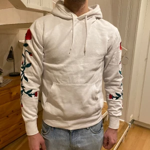 Hoodie - Vit hoodie med rosor på armarna. Storlek XS. Litet hål på armen (se bild) köparen står för frakten.