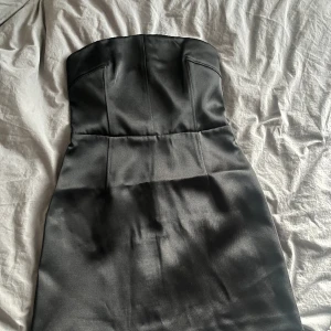 Svart nyårsklänning  - Snygg kort figurnära satinklänning med korsettliknande överdel. Helt ny med prislapp, aldrig använt pga fel storlek. 