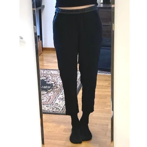 Svarta tygbyxor med läder, 36 S, straight, narrow, enkla, slacks - Svarta byxor i vävt tyg med detaljer i fuskläder, två sidfickor, fuskficka bak. Mått i cm: midja 36; höft 52; benvidd nedanför grenen 28,5; benöppning 14; grenhöjd fram/bak 26/36; innerben 63.