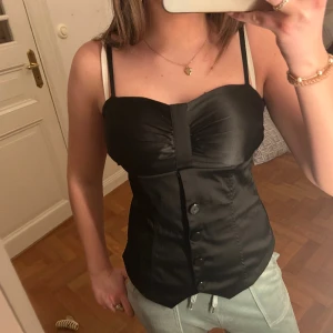 Svart korsett/topp - Svart korsett/ topp med inbyggd vaddering och justerbara band! I ett jättefint silkesliknande material